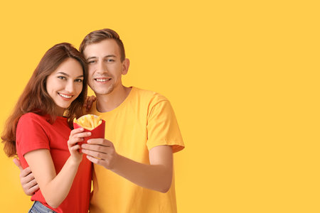 Young couple with french fries on color backgroundの写真素材
