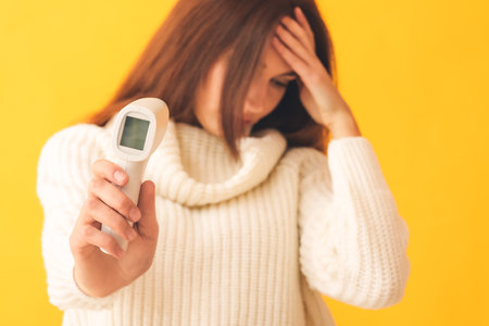 Ill woman with infrared thermometer on color background