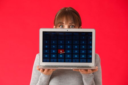 Stressed young woman with laptop on color background. concept of deadlineの写真素材