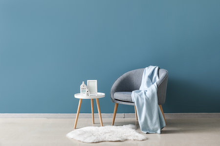 House candle holders on end table, armchair and fur rug near blue wallの写真素材