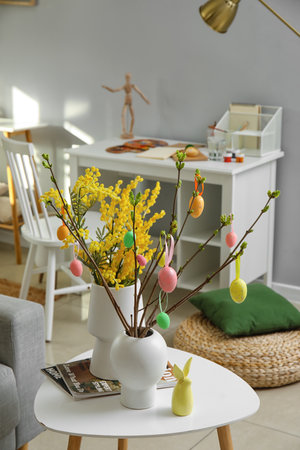 Vases with beautiful Easter decor, mimosa flowers and magazines on table in room