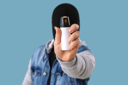 Thief with pepper spray for self-defence on blue background, closeup