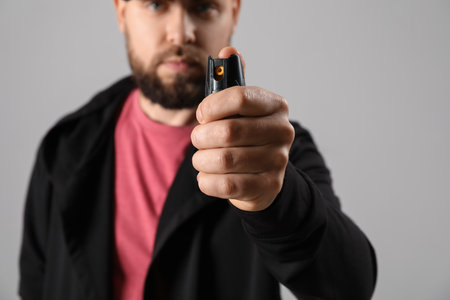 Young man with pepper spray for self-defence on gray background, closeupの写真素材