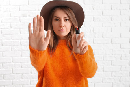 Young woman with pepper spray for self-defence showing STOP gesture on white brick backgroundの写真素材