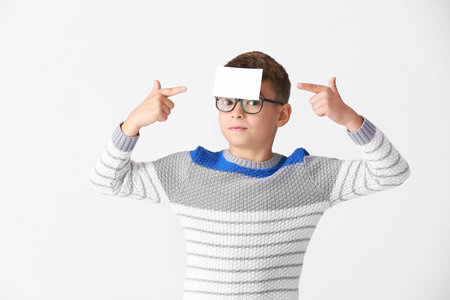 Boy with blank note paper on his forehead against light backgroundの写真素材