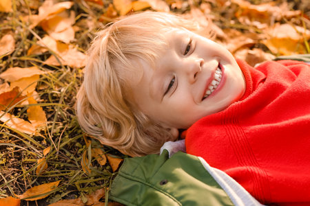 Cute little boy lying on grass in autumn park