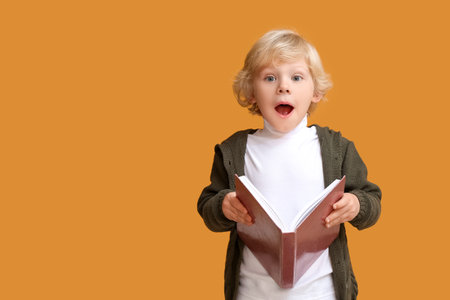 Surprised little boy with book on color background