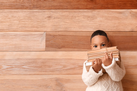 Cute African-American boy with stack of books on wooden backgroundの写真素材