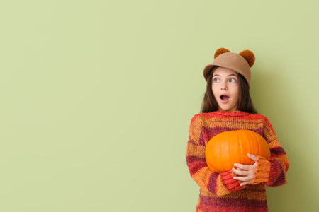 Surprised little girl in autumn clothes and with pumpkin on color backgroundの写真素材