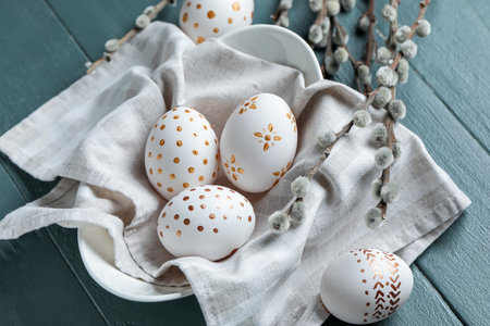 Bowl of painted Easter eggs and willow branches on color wooden background, closeup