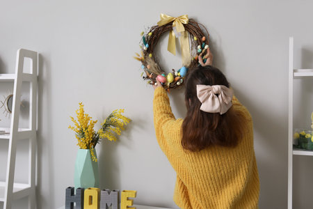 Woman hanging Easter wreath on light wall in living room, back viewの写真素材
