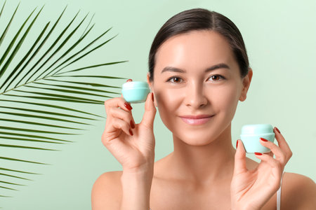 Beautiful young woman with cosmetic products and tropical leaf on color background, closeupの写真素材