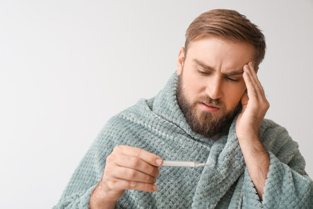 Ill man measuring his temperature on light background