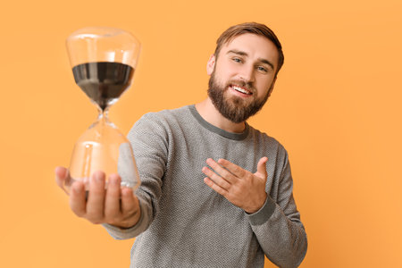 Young man with hourglass on color background