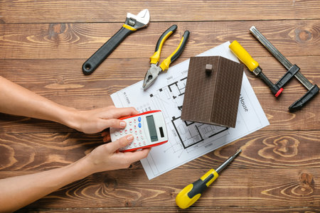 Female hands with model of house and construction tools on wooden background