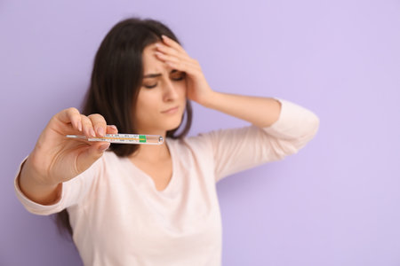 Sick young woman with thermometer on color background
