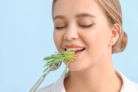 Young woman eating wheatgrass on color backgroundの写真素材