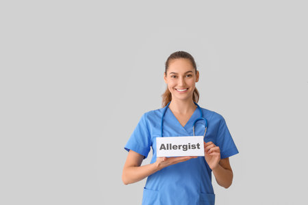Doctor holding paper with word ALLERGIST on light backgroundの写真素材