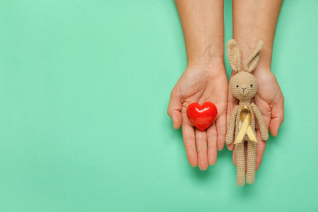 Hands with red heart, toy and golden ribbon on color background. Childhood cancer awareness conceptの写真素材