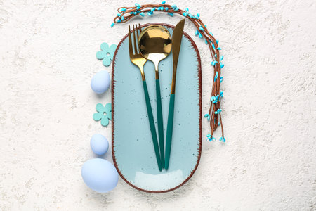 Table setting with Easter eggs, cutlery and floral decor on white grunge background