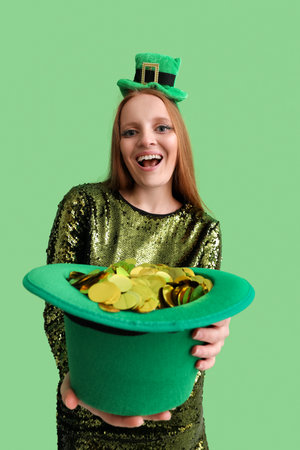 Beautiful redhead woman with hat of confetti on green background. St. Patrick's Day celebration