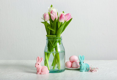 Vase with beautiful tulip flowers, Easter eggs and bunnies on light backgroundの写真素材