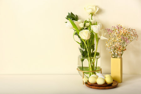 Vases with beautiful flowers and plate of painted Easter eggs on color backgroundの写真素材