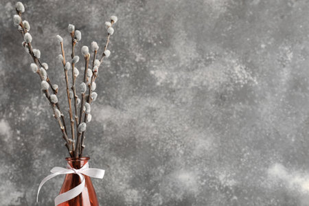 Vase with pussy willow branches and white ribbon on gray grunge table
