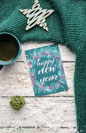 Beautiful greeting card for New Year celebration, cup of tea and sweater on white wooden backgroundの写真素材