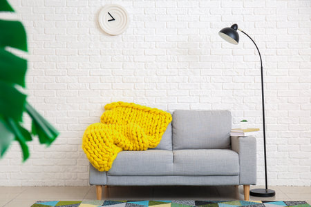 Stylish sofa with knitted plaid near color wall in roomの写真素材