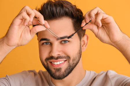 Young man with tools for eyebrow correction on color background