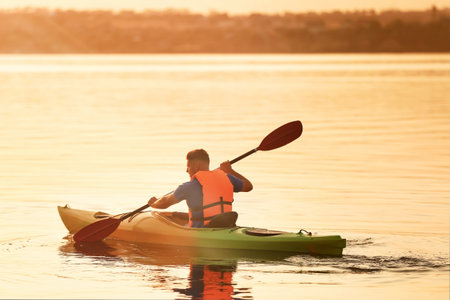 Young man kayaking in the river at sunsetの写真素材