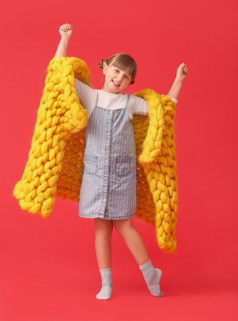 Happy little girl with warm plaid on color backgroundの写真素材