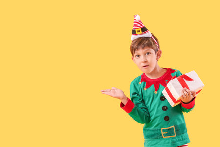 Cute little elf with Christmas gift showing something on color backgroundの写真素材