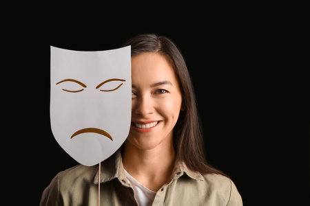 Happy actress with sad mask on dark backgroundの写真素材