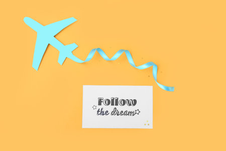 Paper sheet with text FOLLOW YOUR DREAMS and airplane on color background
