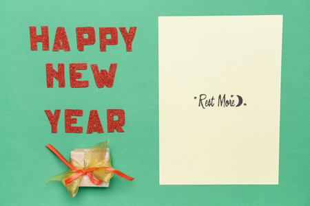 Paper sheet with text REST MORE and HAPPY NEW YEAR on color background