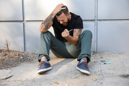 Depressed male junkie sitting outdoors. concept of addiction