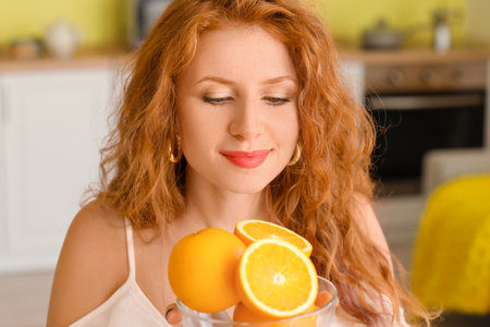 Beautiful young woman with fresh oranges at homeの写真素材