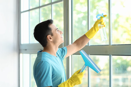 Young man cleaning window at home