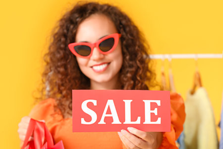 Beautiful African-American woman holding paper with word SALE on color background. Black Fridayの写真素材
