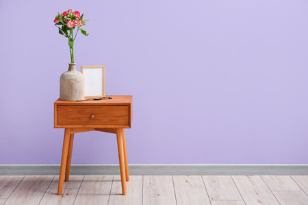 Vase with alstroemeria flowers, blank frame and wristwatch on table near lilac wallの写真素材