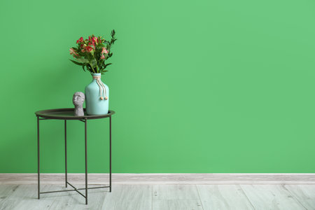Vase with beautiful alstroemeria flowers and decor on table near green wallの写真素材