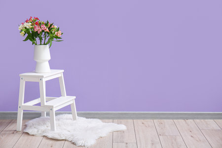 Vase with beautiful alstroemeria flowers on stepladder near lilac wall
