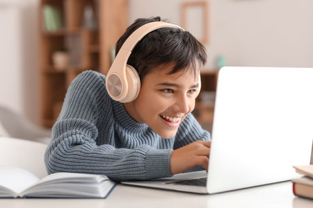Happy little boy in headphones using laptop at homeの写真素材