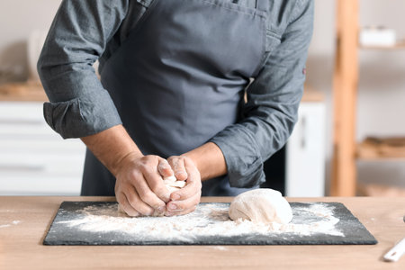 Male baker preparing dough at table in kitchen, closeup