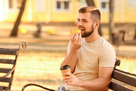 Handsome young man with sweet donut and coffee in parkの写真素材