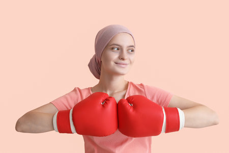 Woman after chemotherapy in boxing gloves on color background. Fight against cancerの写真素材