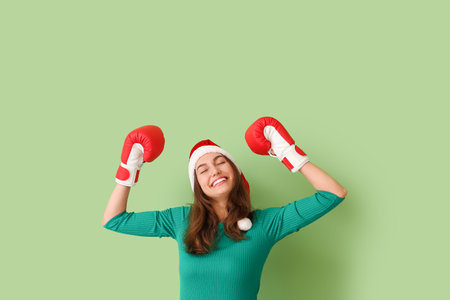 Beautiful young woman in Santa hat and boxing gloves on color background. Boxing day conceptの写真素材