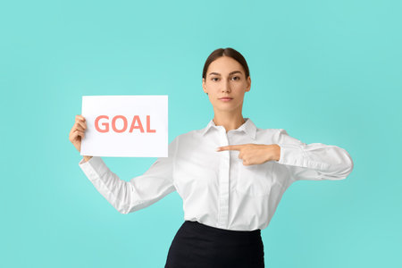 Young businesswoman holding paper with word GOAL on color backgroundの写真素材
